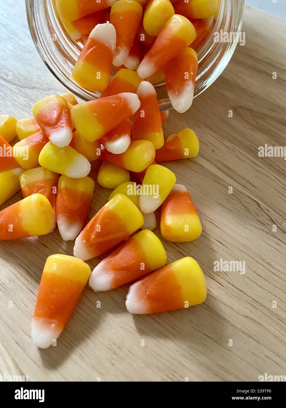Candy corn spilling out of a glass jar onto wooden countertop. - Smartphone Captured Stock Image