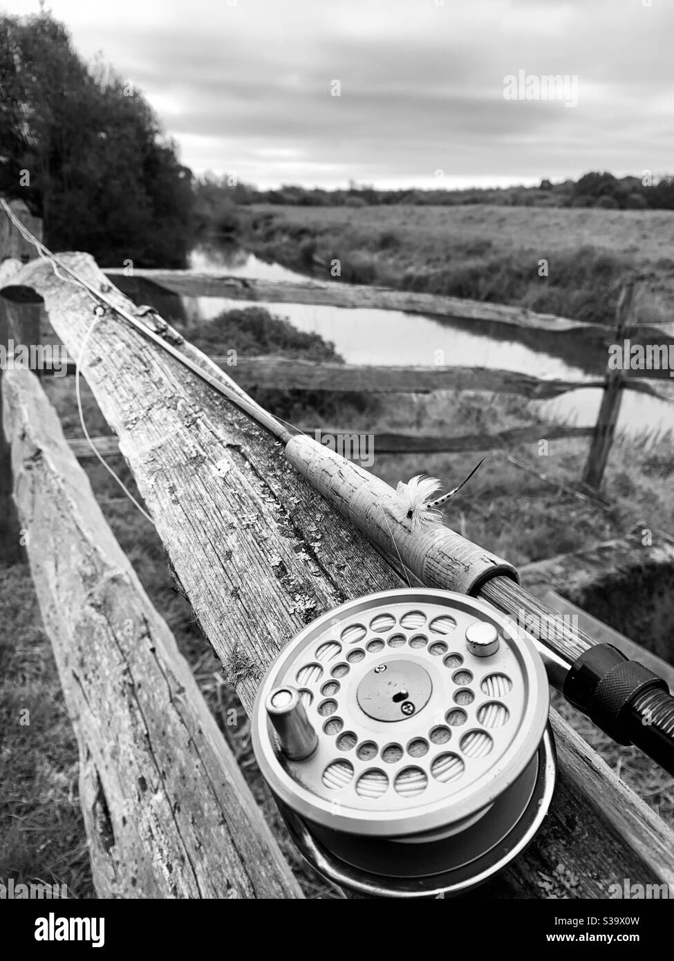 Fly fishing rod and reel with imitation mayfly attached resting on rustic  wooden fence next to river Stock Photo - Alamy