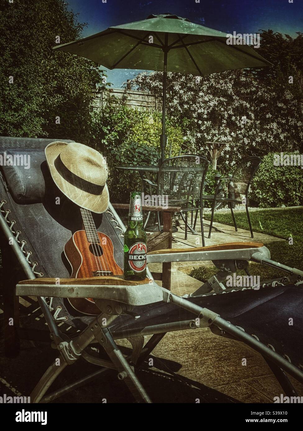 Ukulele straw hat and beer bottle on recliner summertime in the garden Stock Photo