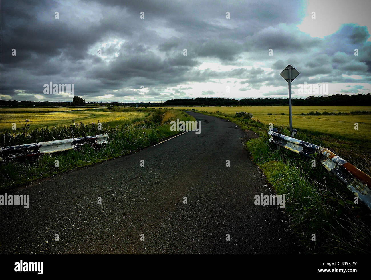 Lonely country lane surrounded by fields with moody skies above Stock Photo