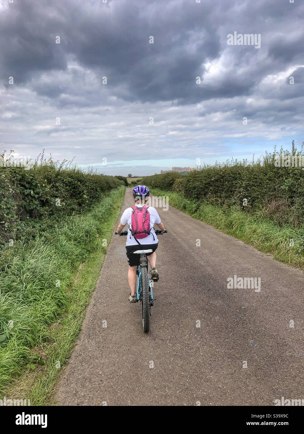 Woman cycling towards Bamburgh Castle Northumberland - Smartphone Captured Stock Image