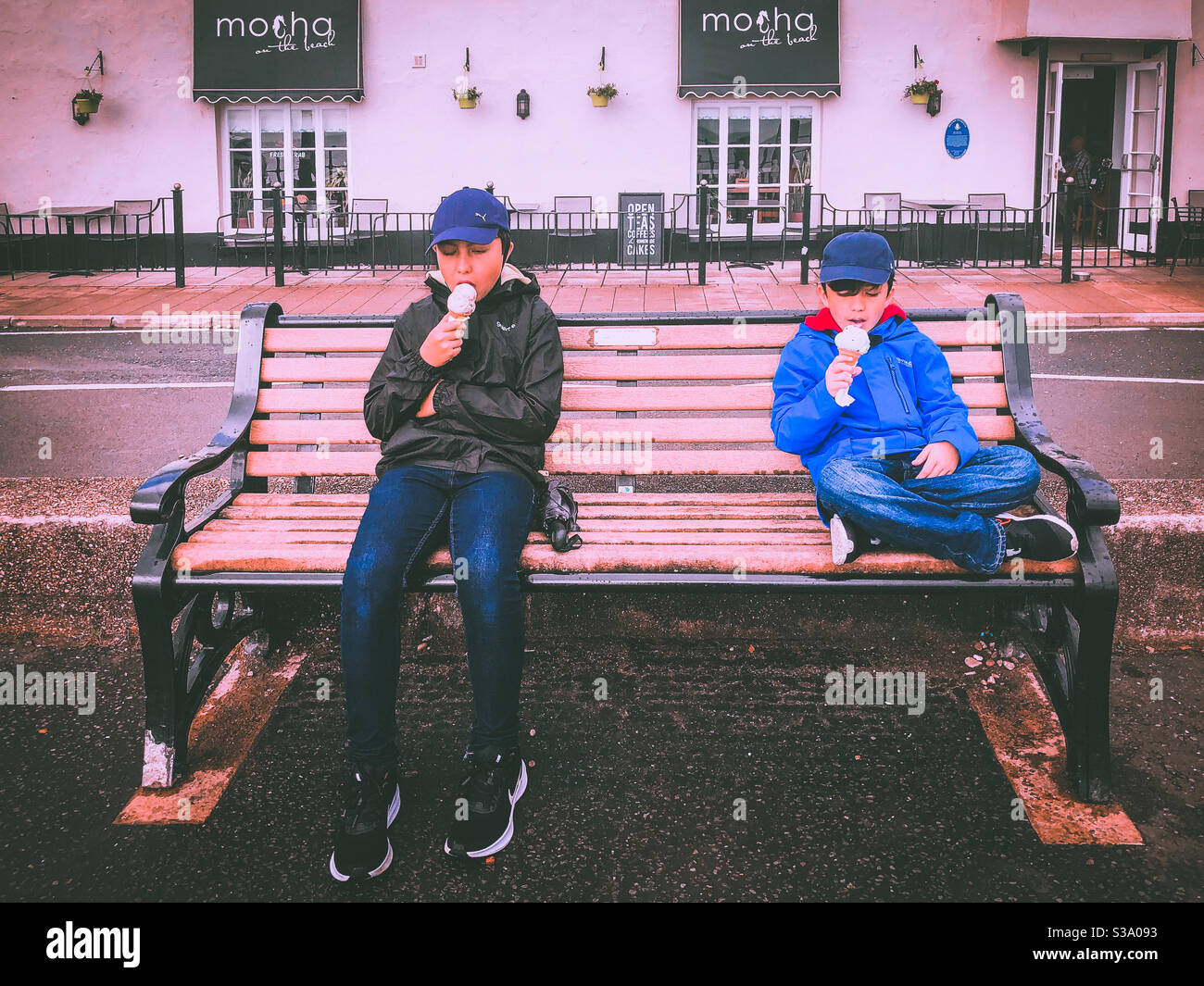 Two brothers sit together in a bench and eat an ice cream. - Smartphone Captured Stock Image