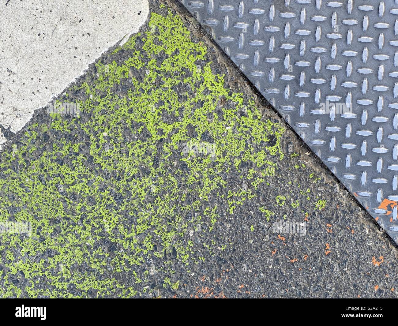 Grunge texture background with green paint on asphalt surface next to patterned metal and concrete - Smartphone Captured Stock Image