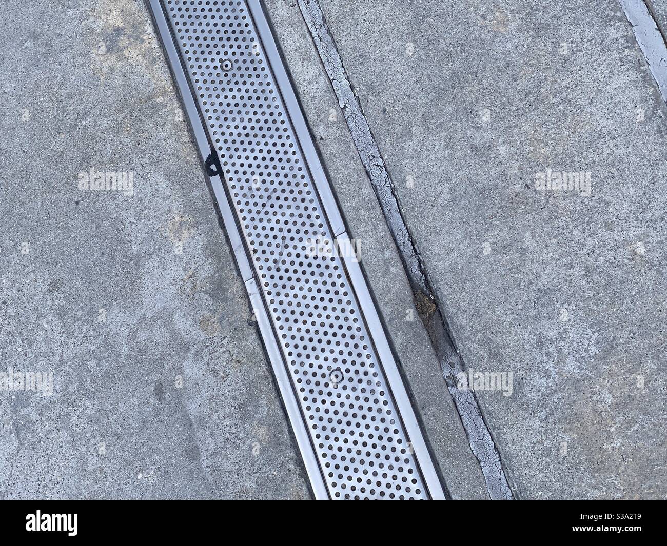 Metal drain cover and concrete creating abstract grunge background, suitable for compositing with text and graphics - Smartphone Captured Stock Image