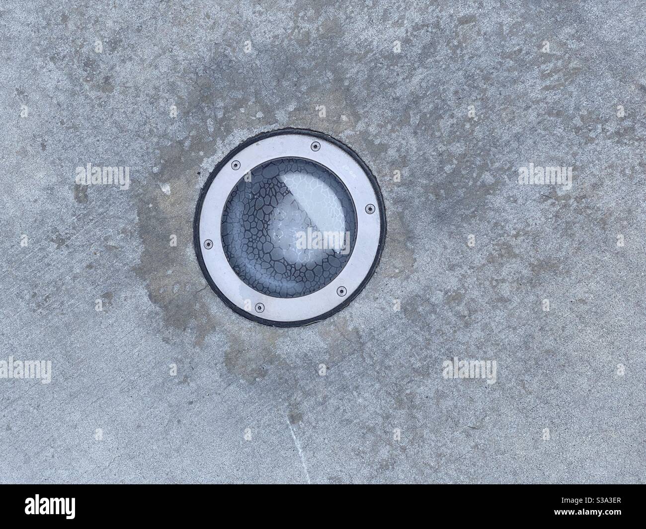 Detail of light with textured glass cover, embedded in concrete sidewalk, creating abstract background texture Stock Photo