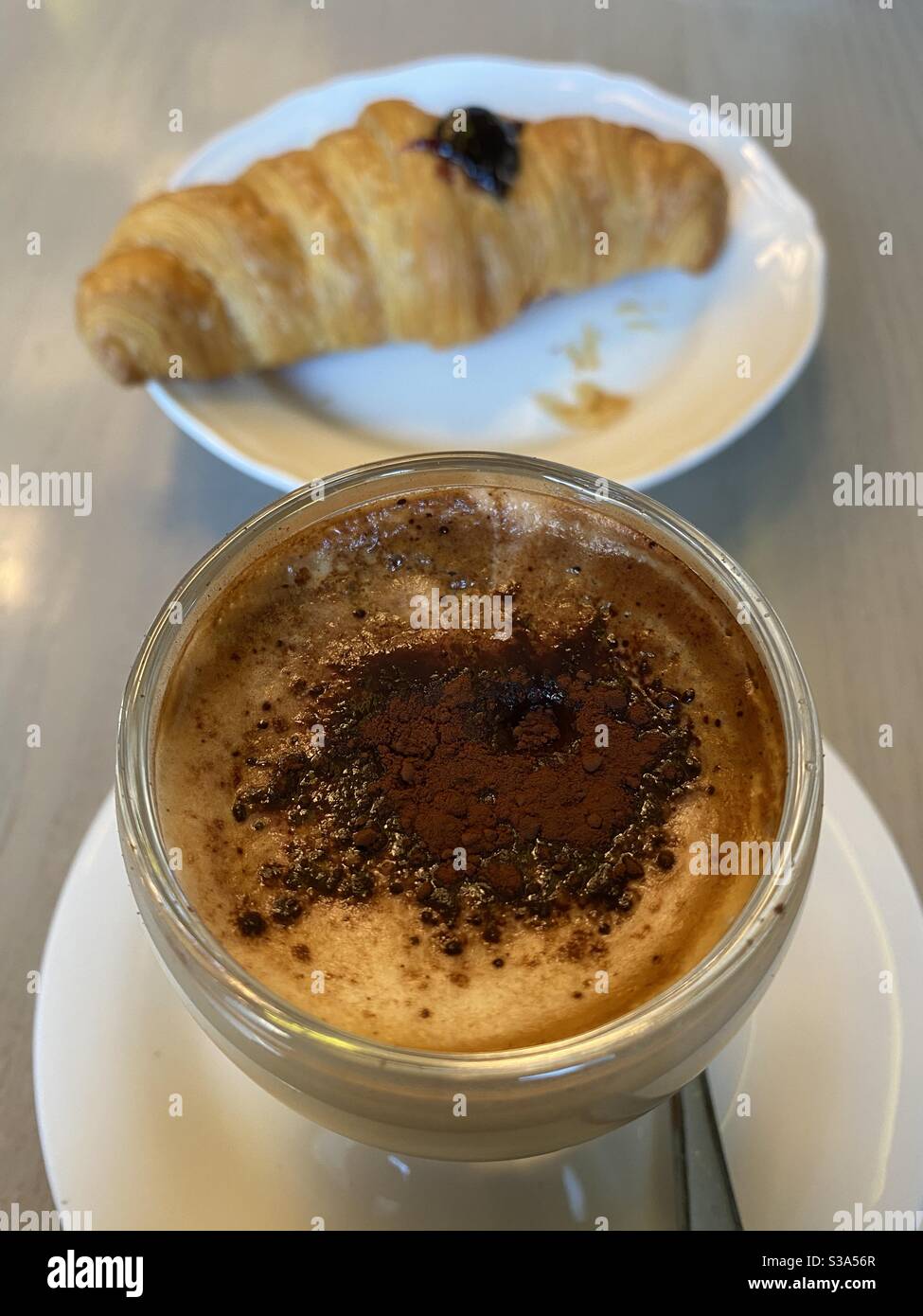 Moretto, espresso hot coffee with milk and chocolate powder and a fresh croissant - Smartphone Captured Stock Image