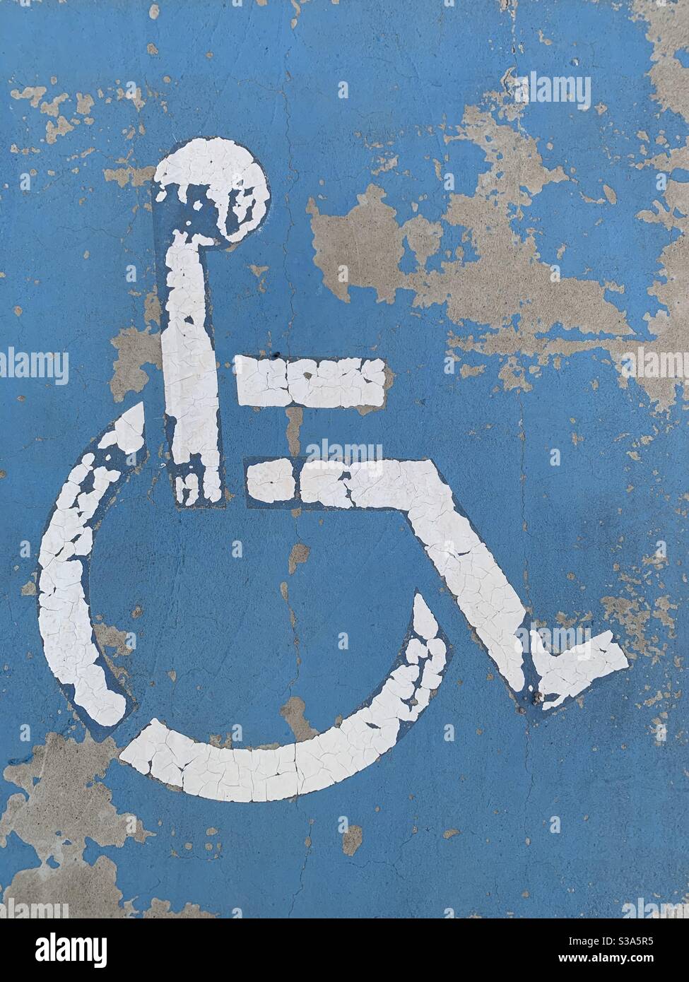 A faded and peeling white painted wheelchair access parking sign painted on a concrete parking space - Smartphone Captured Stock Image