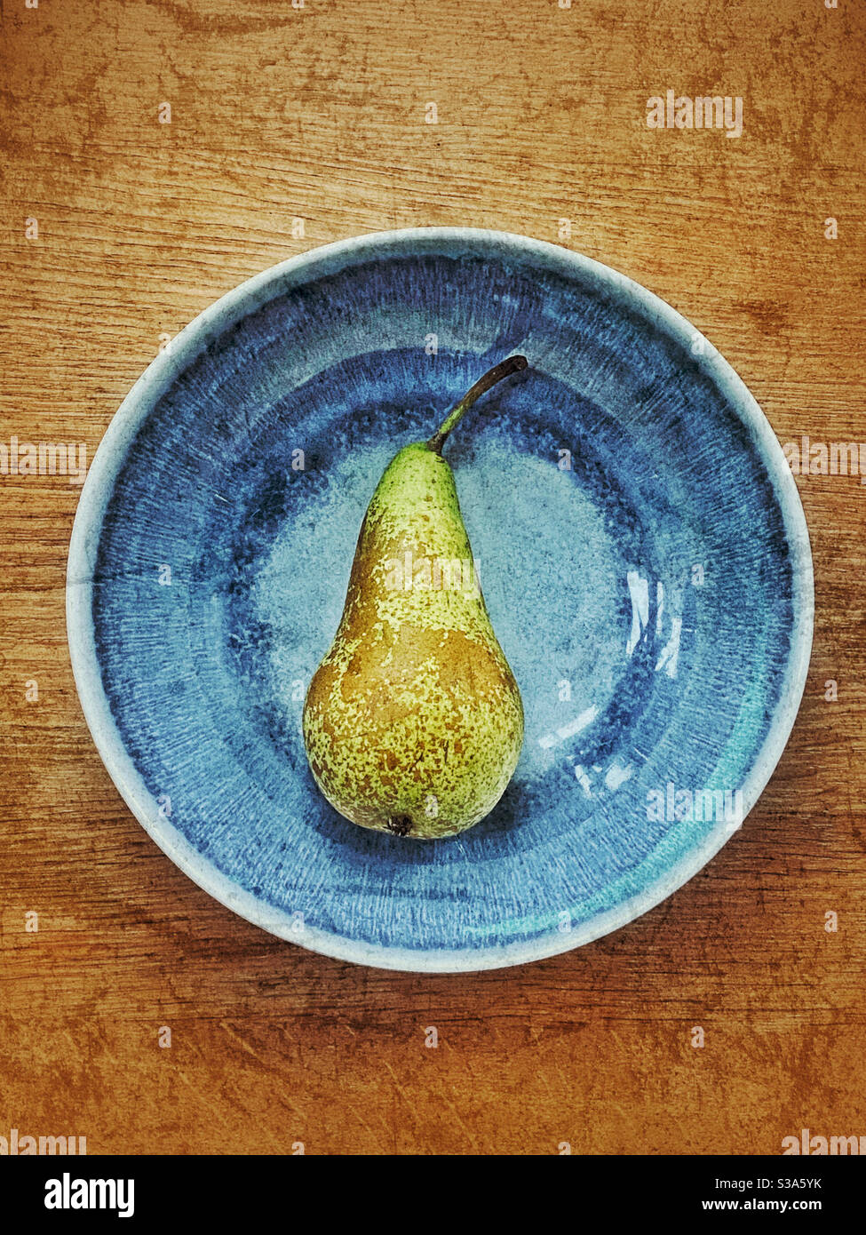 An overhead view of a single Conference Pear (Pyrus Communis) in a mottled blue bowl. Room for copy. Photo Credit - ©️ COLIN HOSKINS. - Smartphone Captured Stock Image