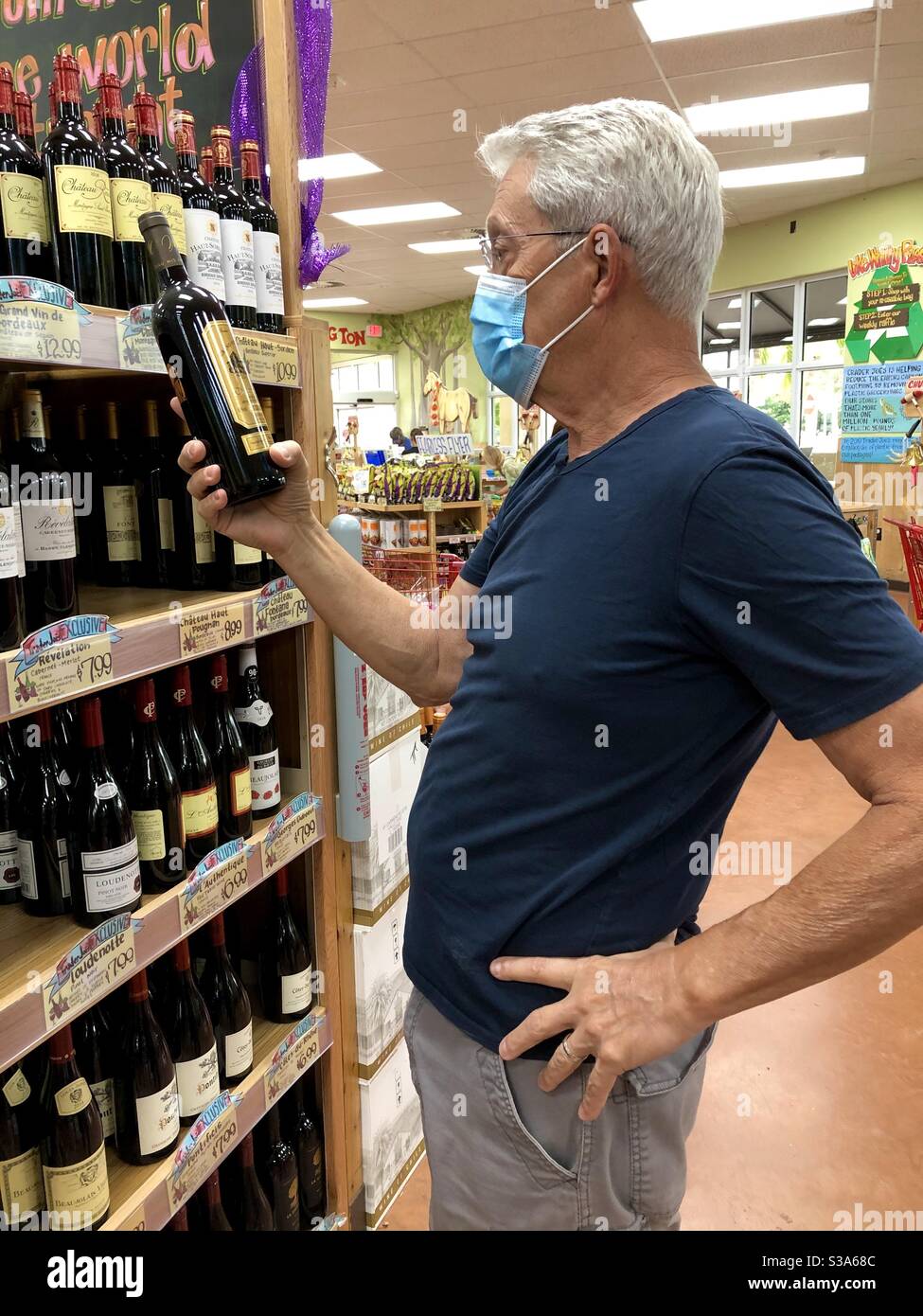 Adult man safely shopping for wine at Trader Joe’s supermarket wearing a non- surgical mask. Stock Photo