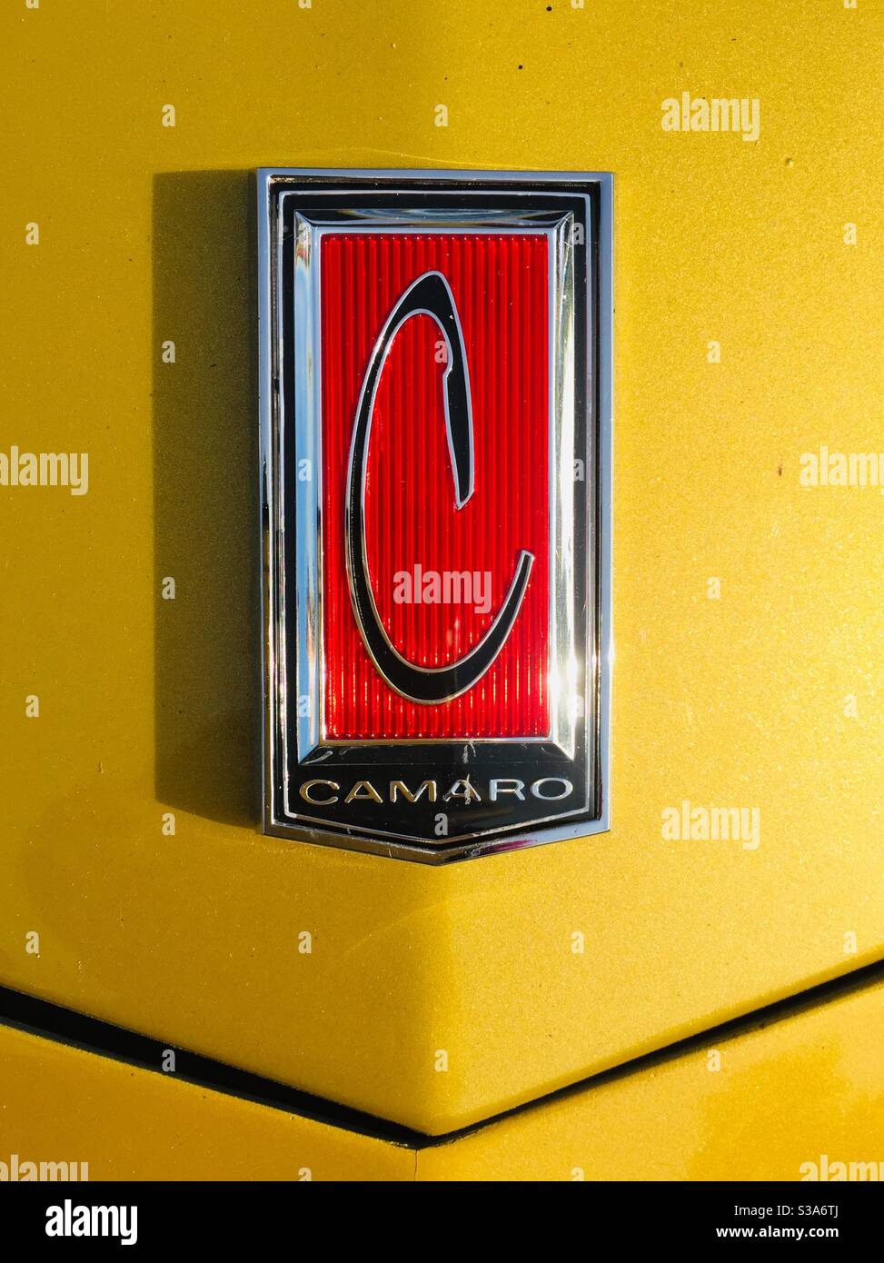 Chevrolet camaro badge.  Black capital C on a red background with chrome on a mustard yellow bonnet Stock Photo