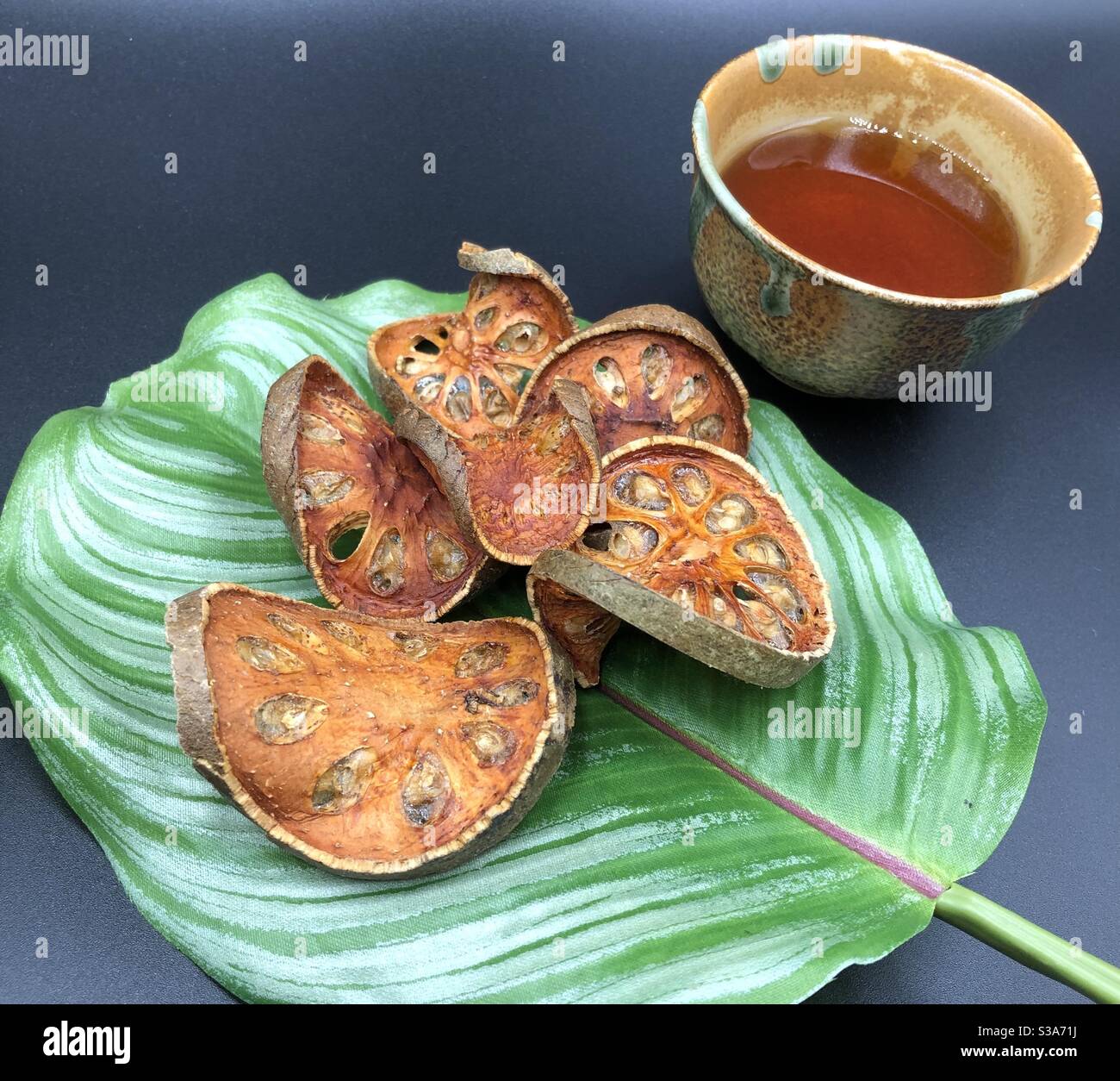 Dried Bael (Aegle marmelos) on green leave side with a cup of bael