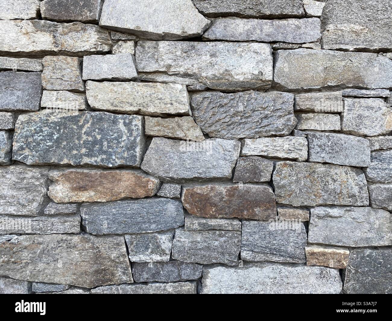 Close view of wall of oddly shaped, grey and other earth-tone bricks made of rock, creating abstract background texture suitable for compositing - Smartphone Captured Stock Image