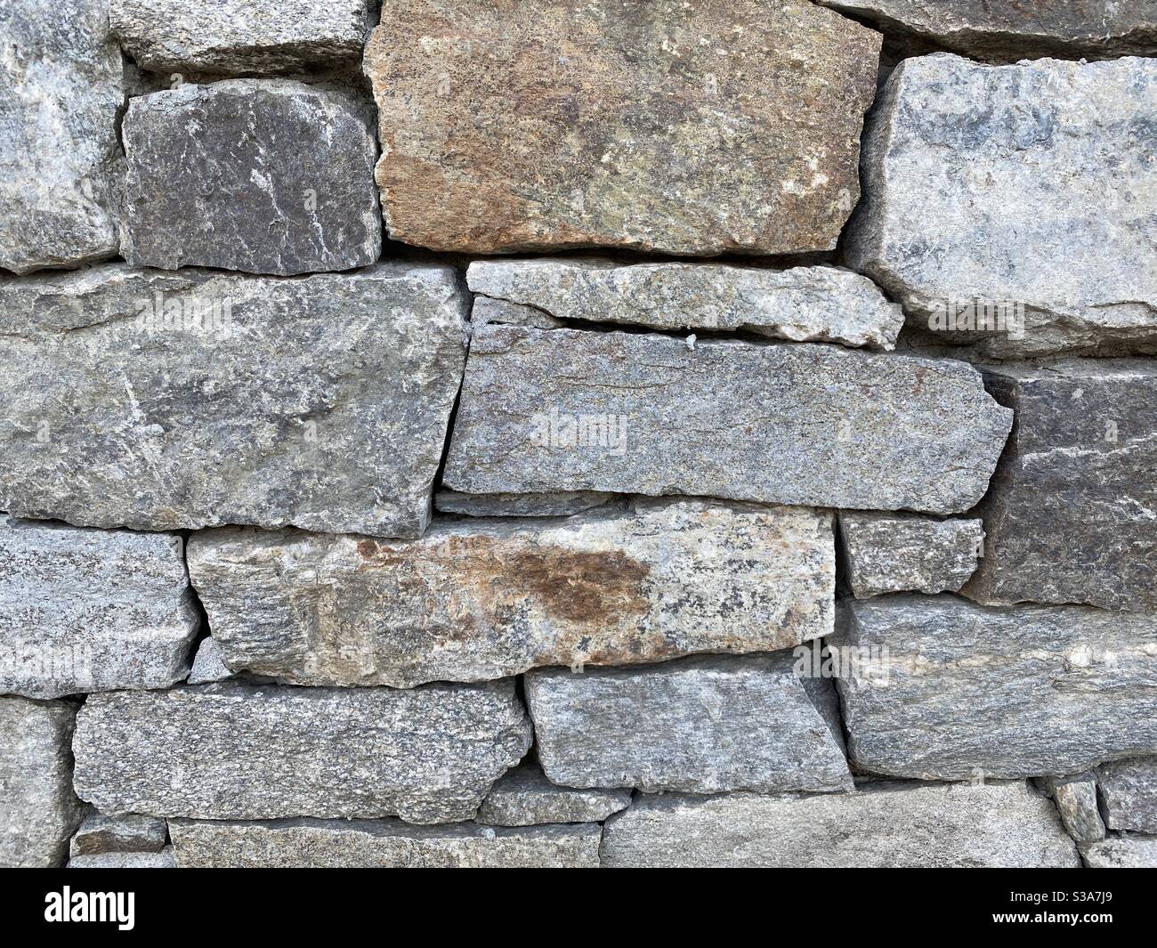 Detail of oddly shaped, grey and other earth-tone bricks in a wall made of rock, creating abstract background texture suitable for compositing - Smartphone Captured Stock Image