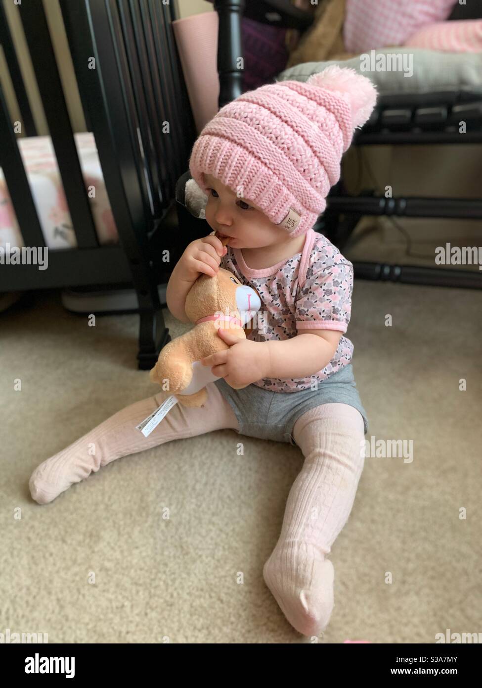 Baby in winter hat chews stuffed animal. Stock Photo
