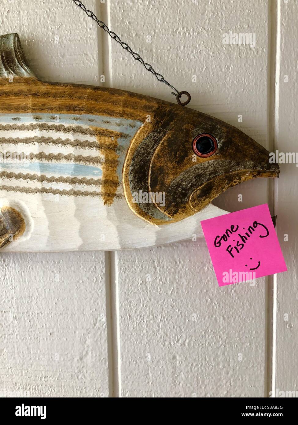 Wooden carved fish on an entry hall wall with a post it note “Gone Fishing.” Stock Photo