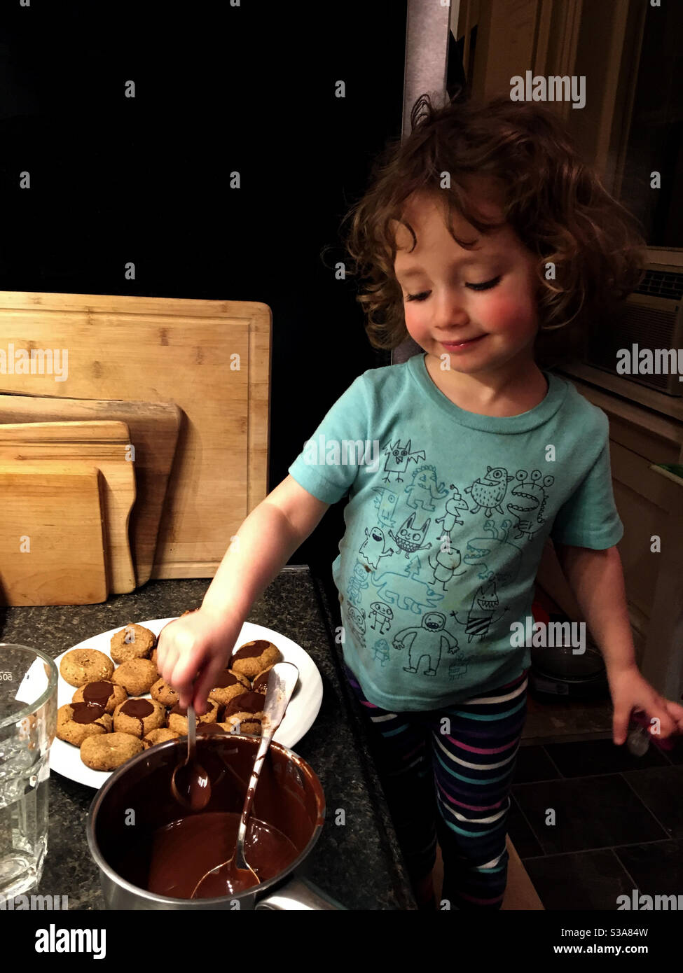 Toddler girl in the kitchen mixing chocolate icing for decorating