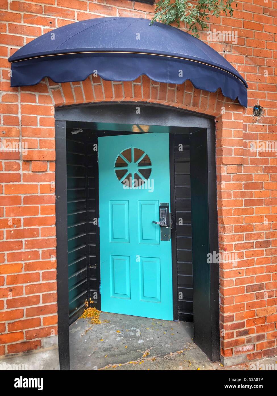 A bright turquoise door as a stark contrast to the red brick building. Stock Photo