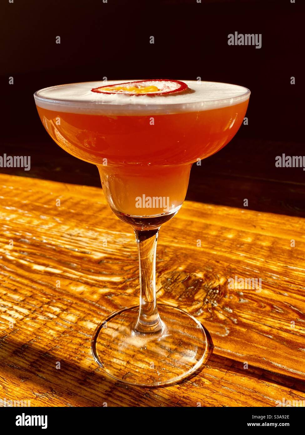 Martini cocktail for Christmas cheer - with a froth top and passion fruit in a long stemmed glass on a wooden table - Smartphone Captured Stock Image