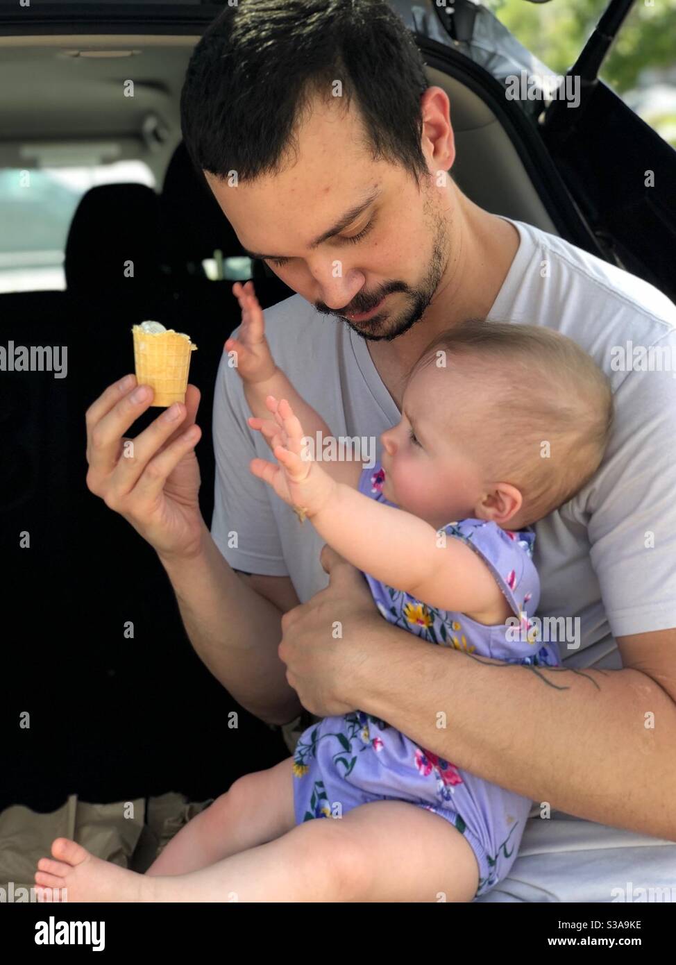 Baby reaching for Dad’s ice cream cone. Stock Photo