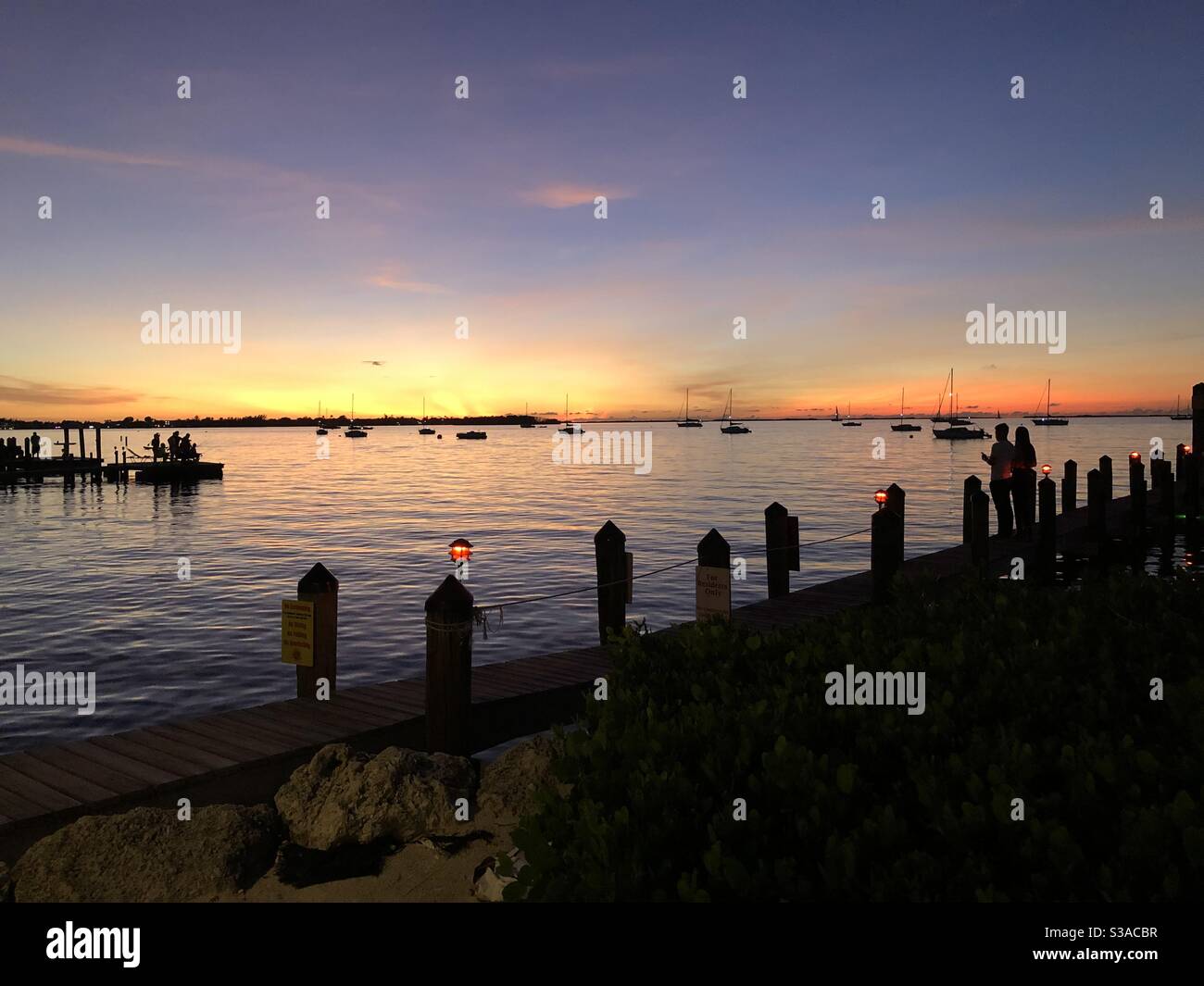 Sunset over bayside with a couple in silhouette standing by a pier in Key Largo, Florida USA. Stock Photo
