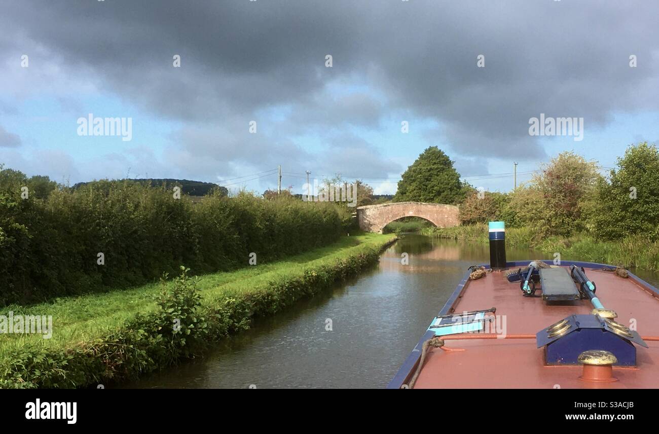 Canal landscape from a boat looking ahead at a bridge in the distance bathed in sunshine with clouds in a blue sky. - Smartphone Captured Stock Image