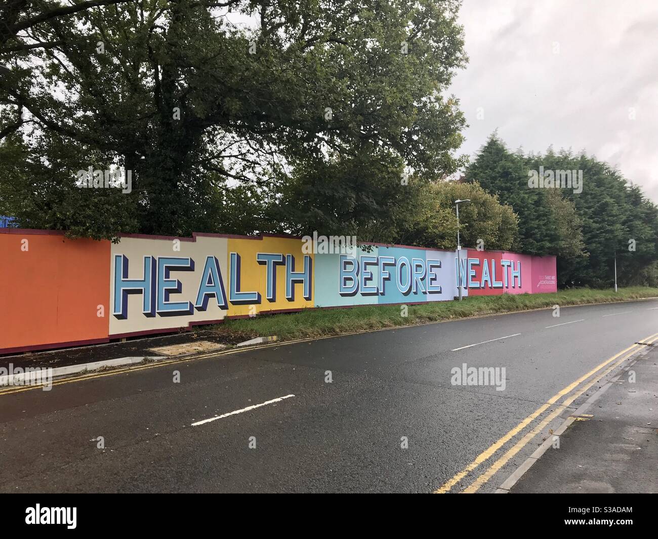 Health before wealth graffiti on hoarding panels near the entrance to Morriston Hospital in Swansea during the Coronavirus pandemic. Stock Photo