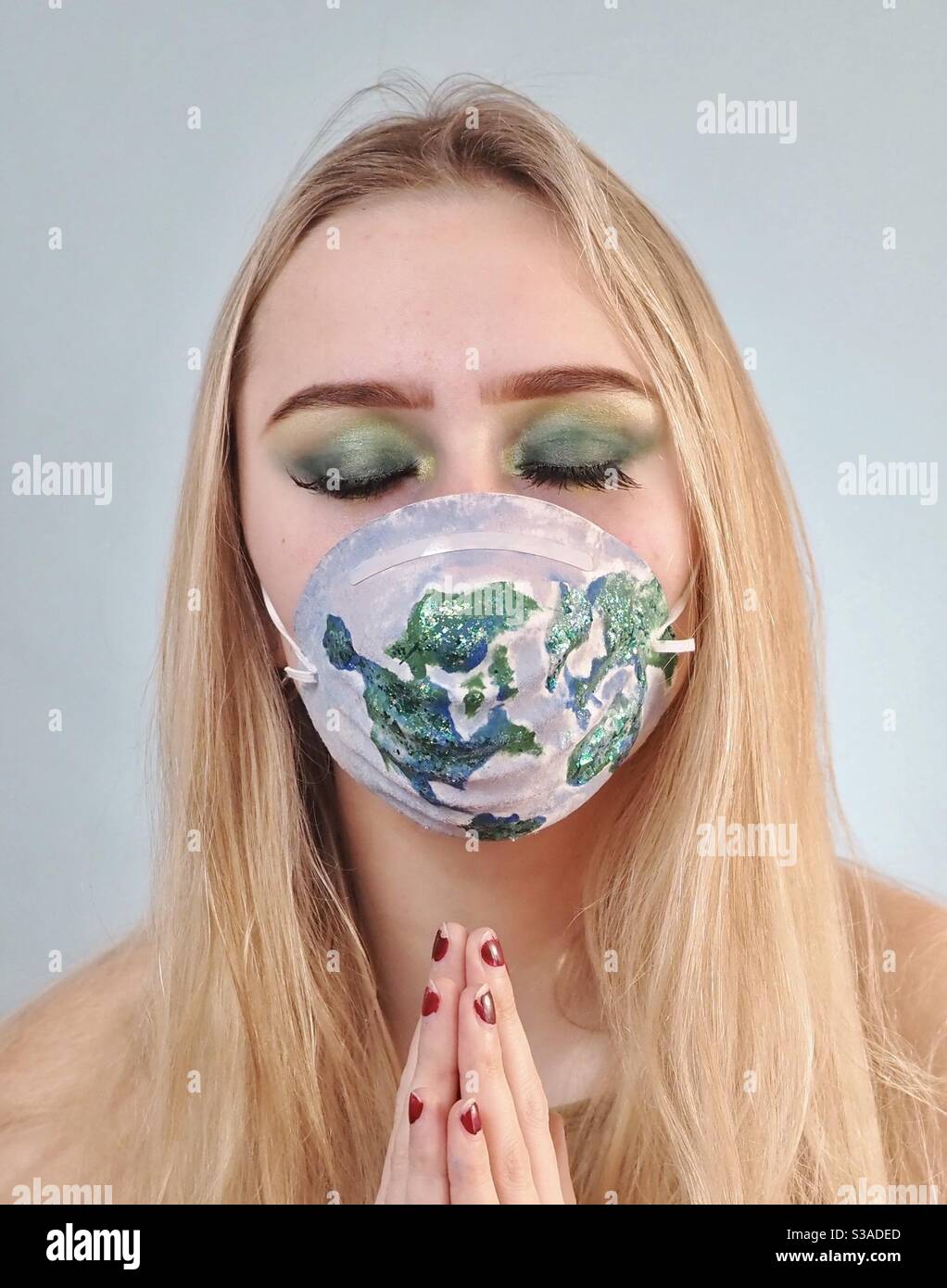 Beautiful young woman, eyes closed wearing protective face mask with map of the world - Smartphone Captured Stock Image