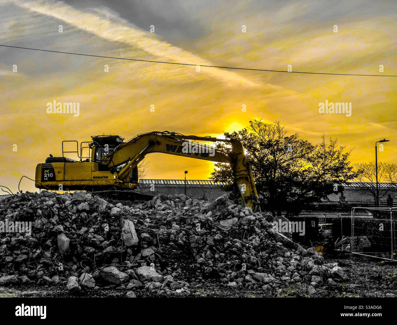 Excavator on top of a pile of rubble on a construction site with setting sun Stock Photo