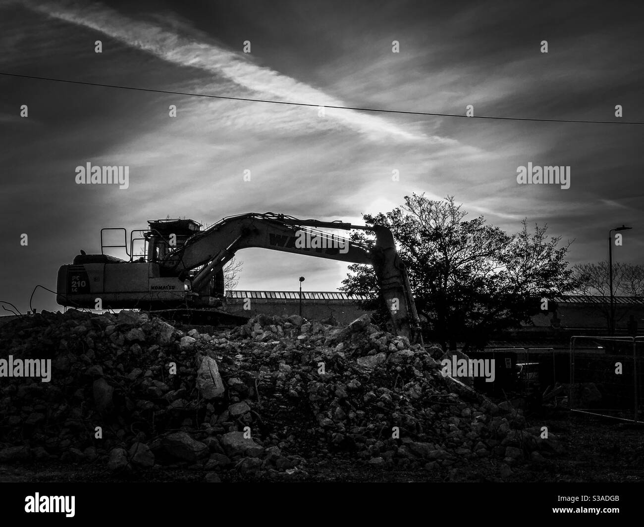 Black and white image of an excavator on top of a pile of rubble on a demolition site Stock Photo