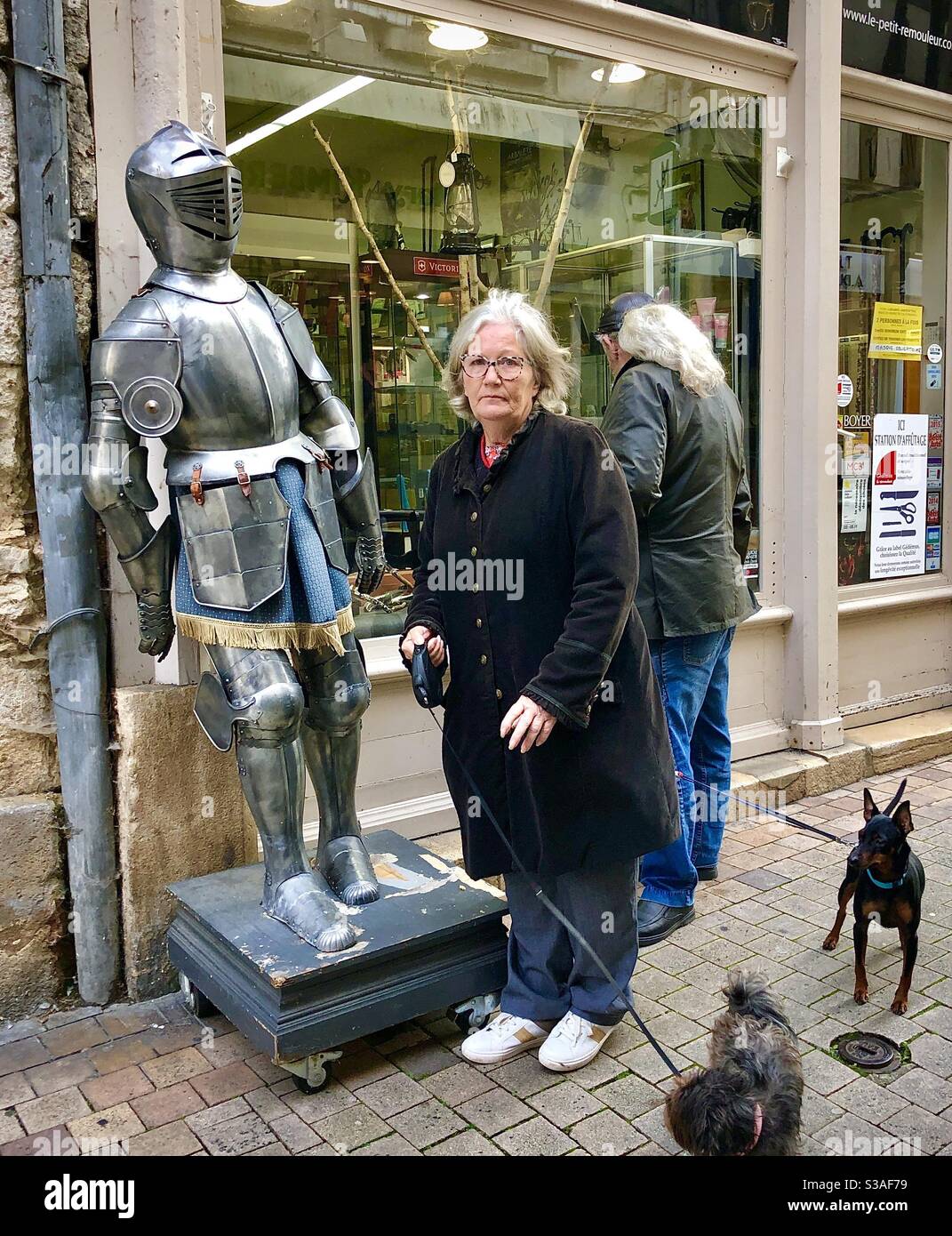 Woman with dogs posing candidly next to a suit of armour display in Bourges, central France. Stock Photo