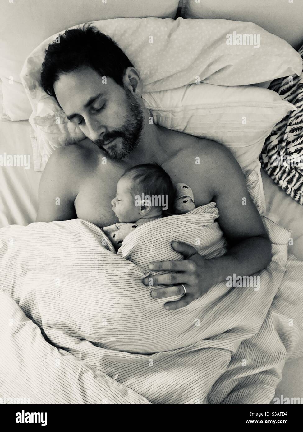 Father in bed holding and bonding with his newborn child. - Smartphone Captured Stock Image