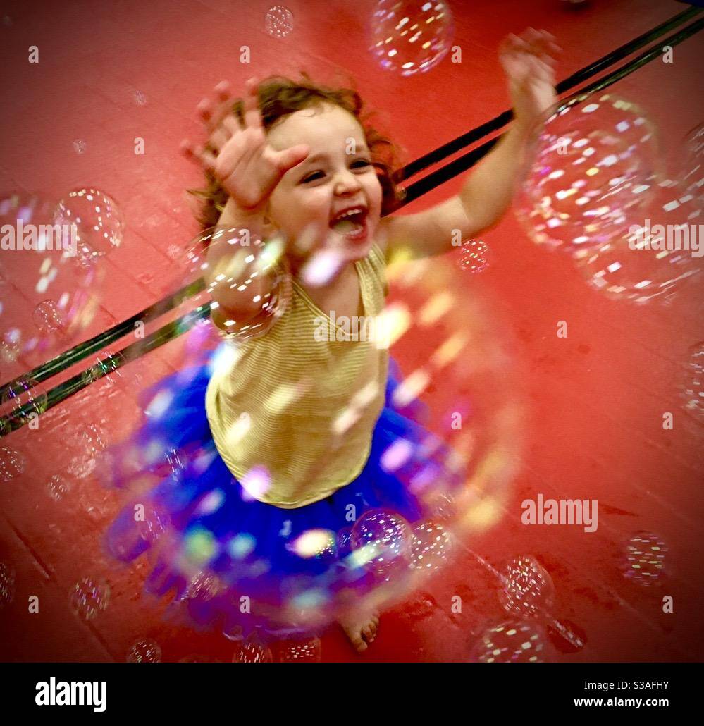 Three year old toddler girl playing with bubbles and wearing a ballet tutu dress. - Smartphone Captured Stock Image
