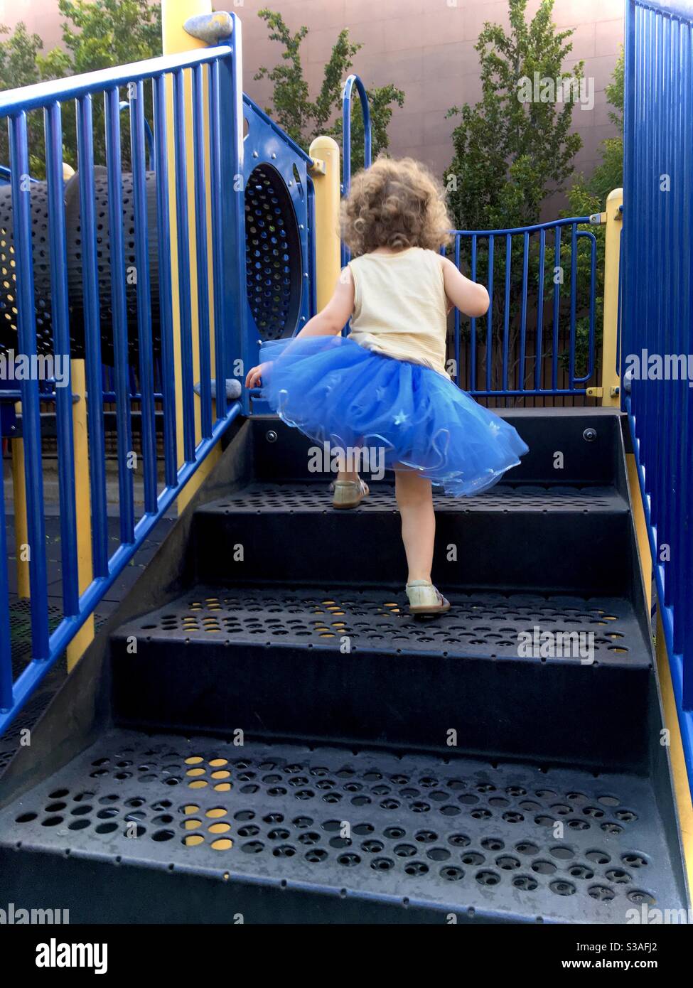 Toddler girl climbing up steps from behind and wearing a blue tutu dress. - Smartphone Captured Stock Image