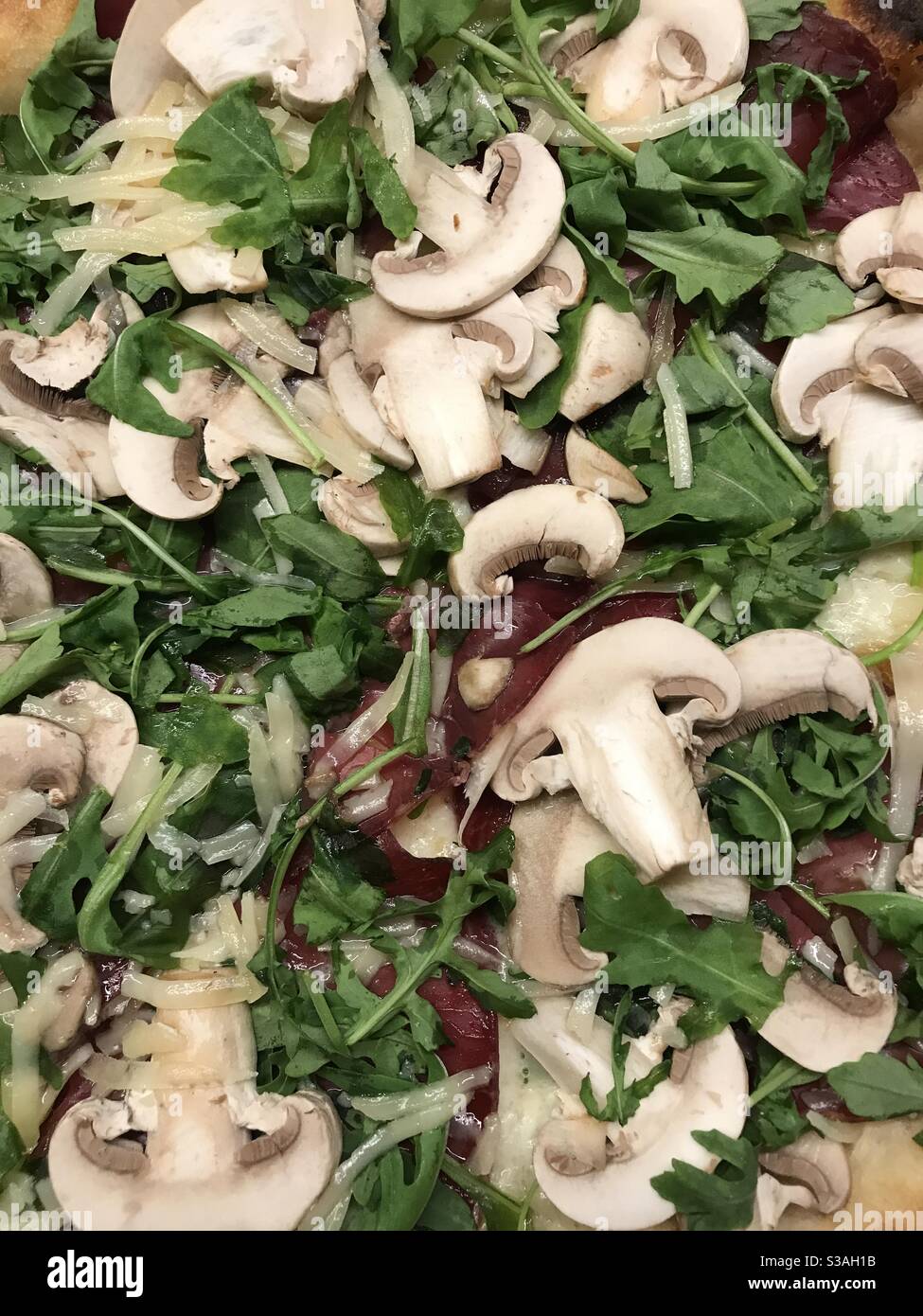 Close up image of a Valtellina pizza topped with bresaola, rocket, fresh mushrooms and shavings of grana cheese - Smartphone Captured Stock Image