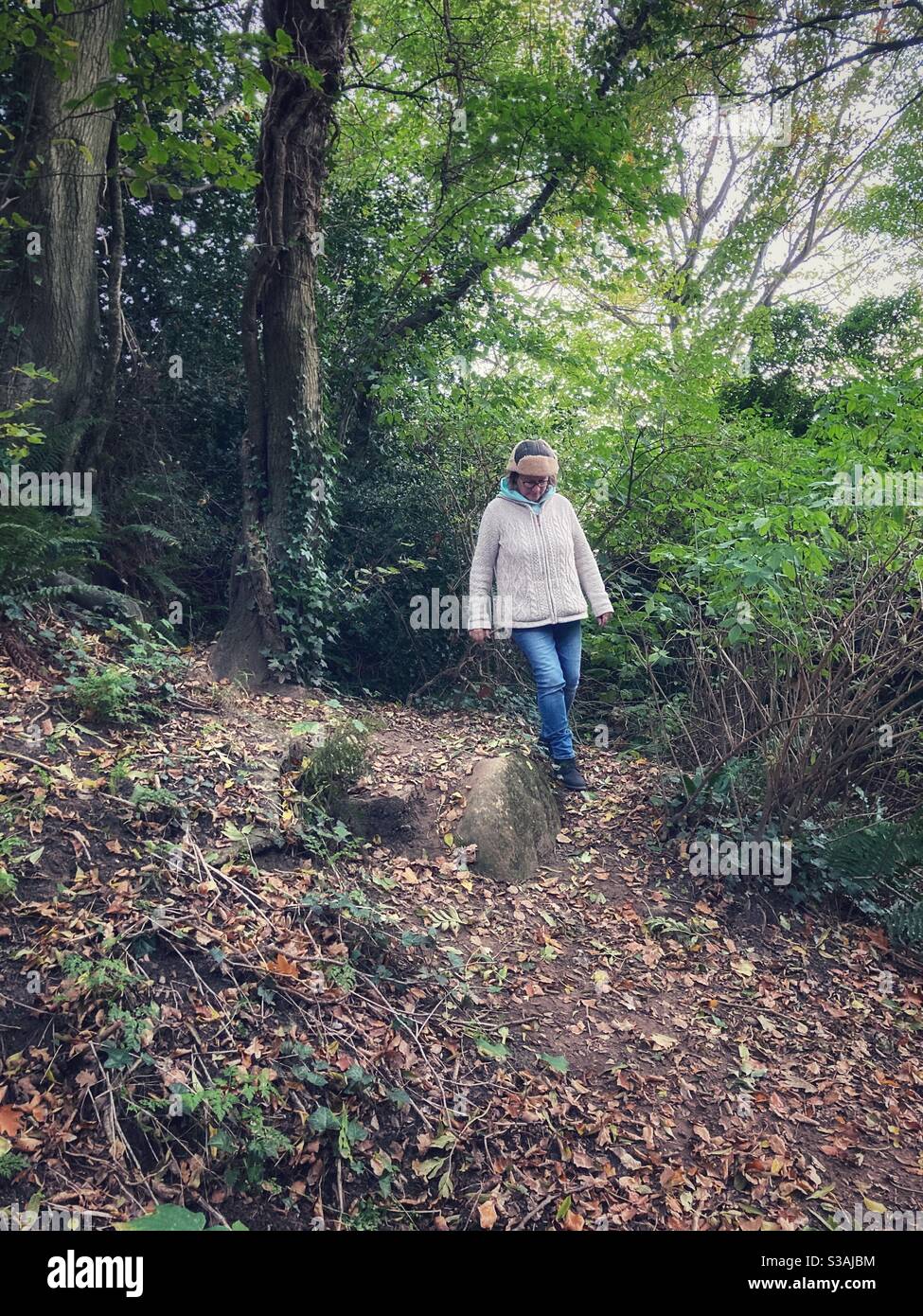 Woman walking down a steep track through woodland  in autumn. Stock Photo