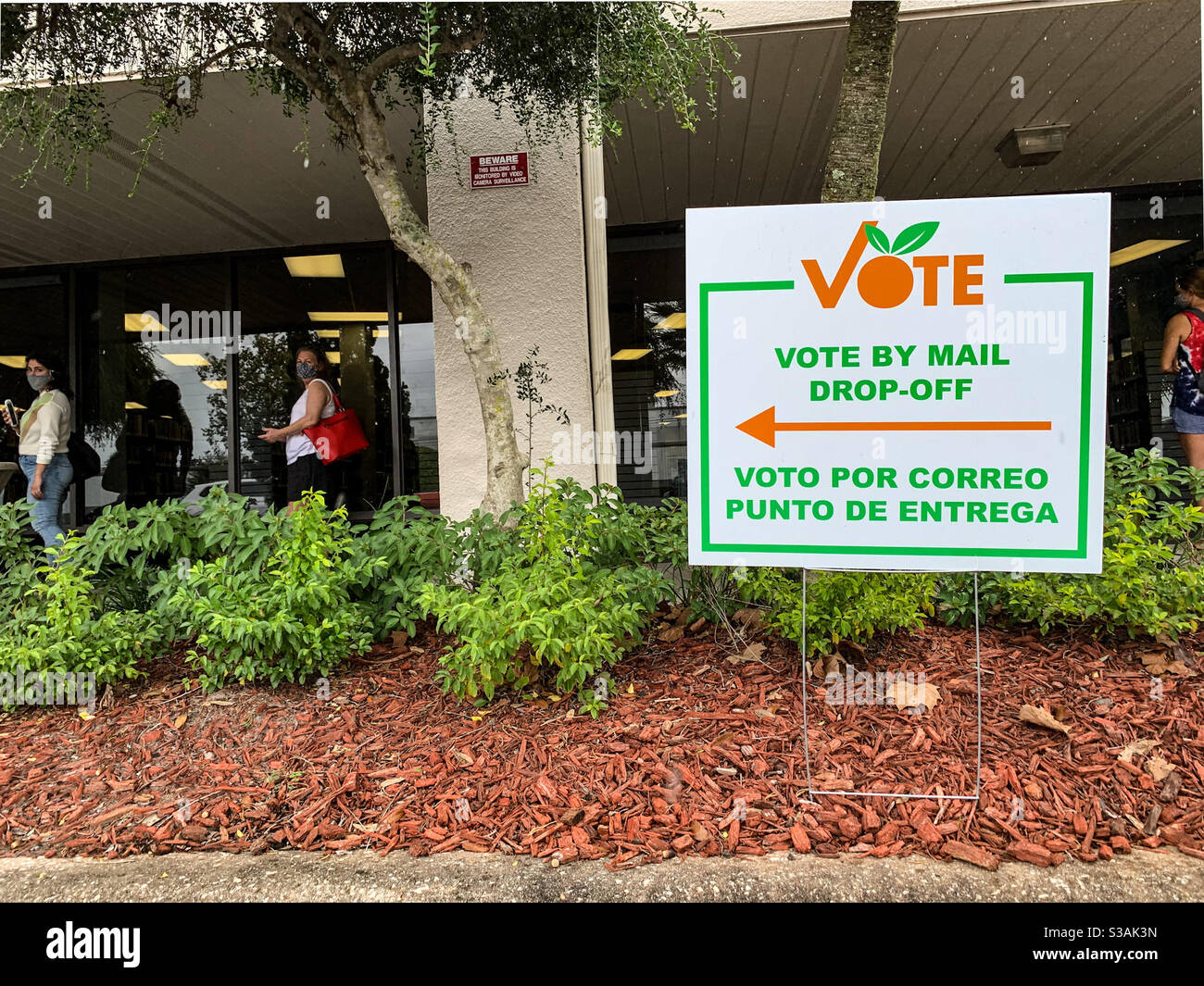 A vote by mail drop off sign in English and Spanish stands in front of a line of masked voters who are also social distancing at an early voting site in Orlando, Florida. Voto por correo. Stock Photo
