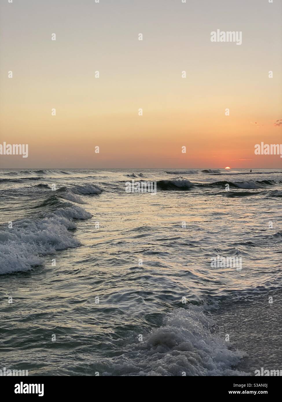 Golden sun nearly completely set over the Gulf of Mexico water with a silhouette person in the water - Smartphone Captured Stock Image
