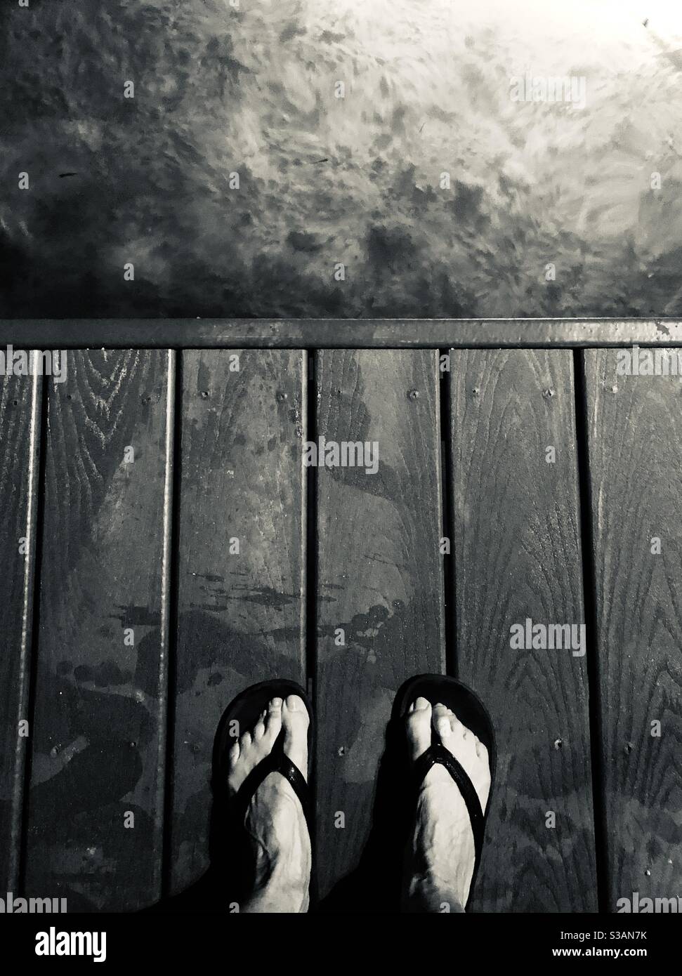 Feet standing on a dock looking into the dark water. - Smartphone Captured Stock Image