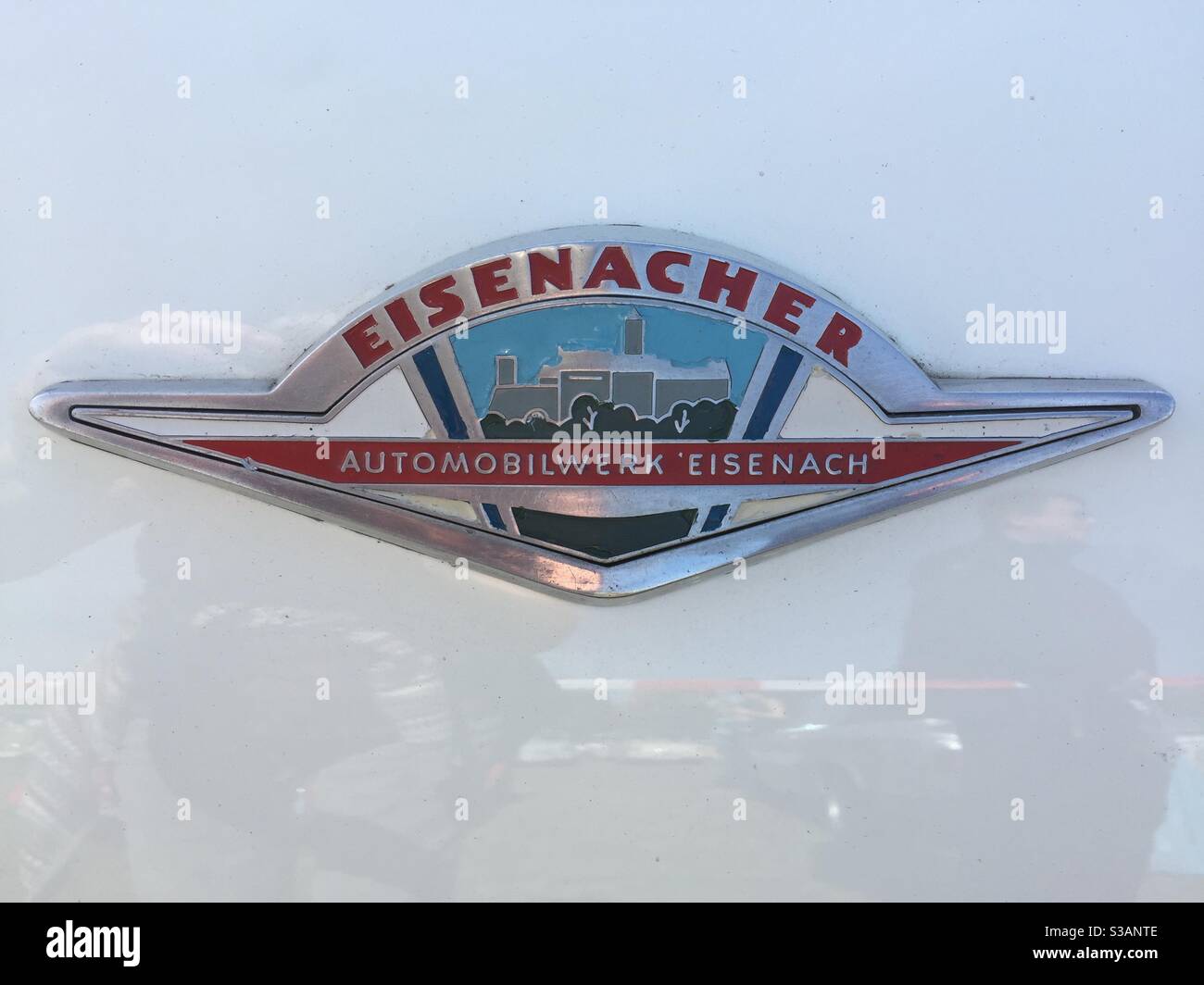 Chrome badge on a Wartburg 311 from Automobilwerk Eisenach.  Red lettering with grey and blue townscape  on a cream coloured chassis Stock Photo