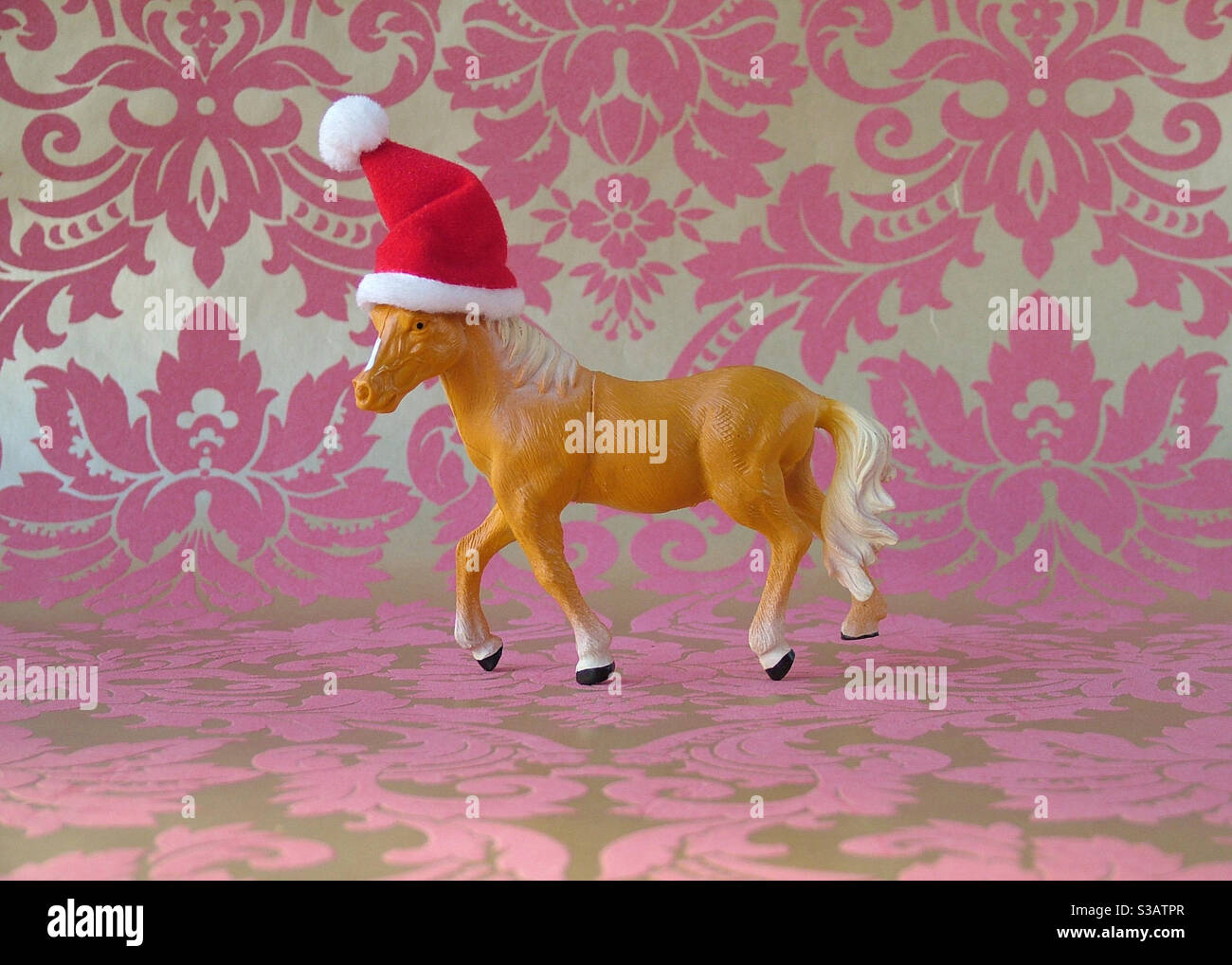 Plastic toy horse with Santa Hat on pink and gold Arabesque wallpaper