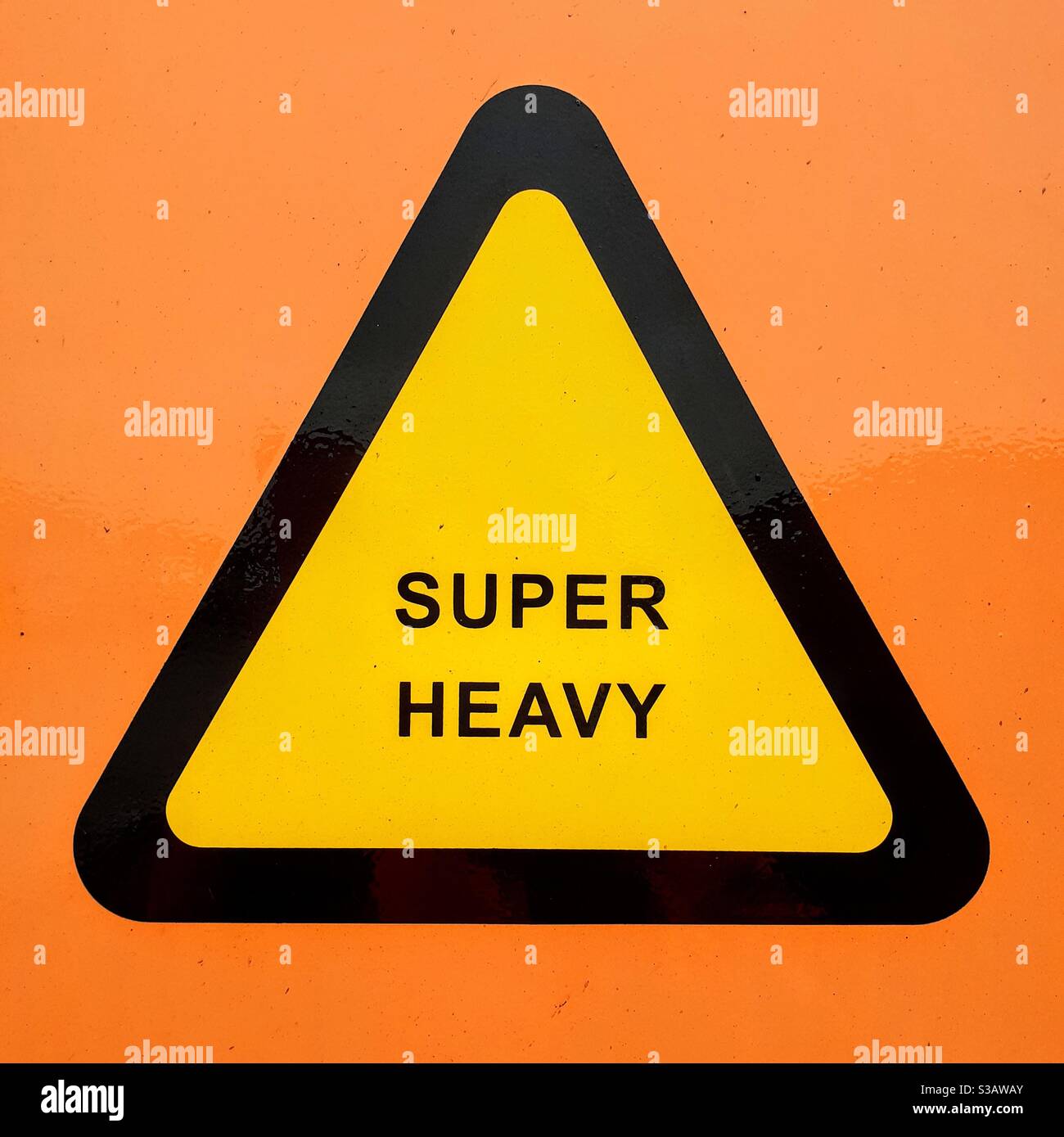 A yellow triangular warning sign informing the bearer of a super heavy weight on the side of an industrial shipping container or cargo box - Smartphone Captured Stock Image