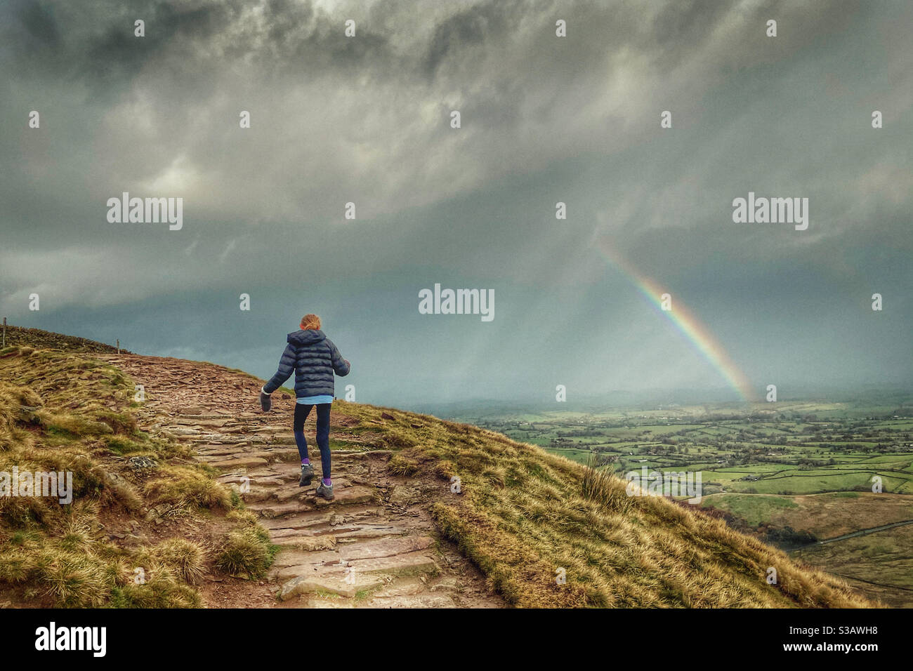 Girl walking up Pendle Hill with rainbow over fields in distance - Smartphone Captured Stock Image