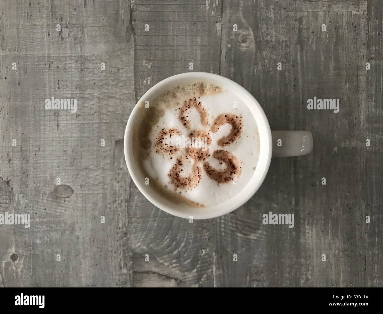 Flower shaped design on a cup of cappuccino coffee - Smartphone Captured Stock Image