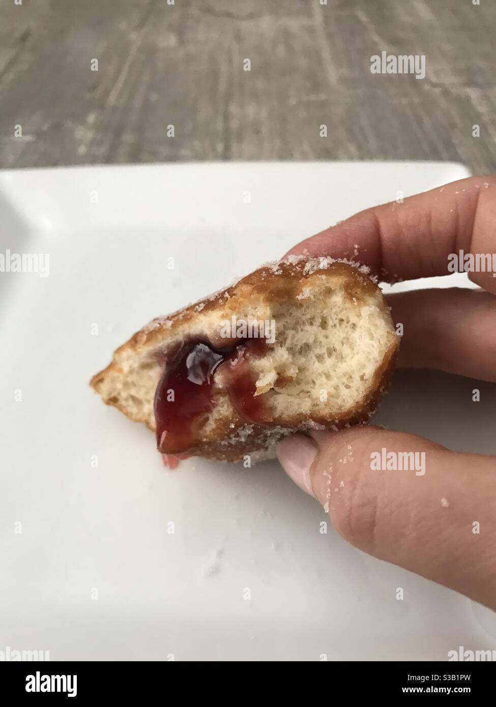 Lady holding a half eaten jam doughnut in her hand - Smartphone Captured Stock Image
