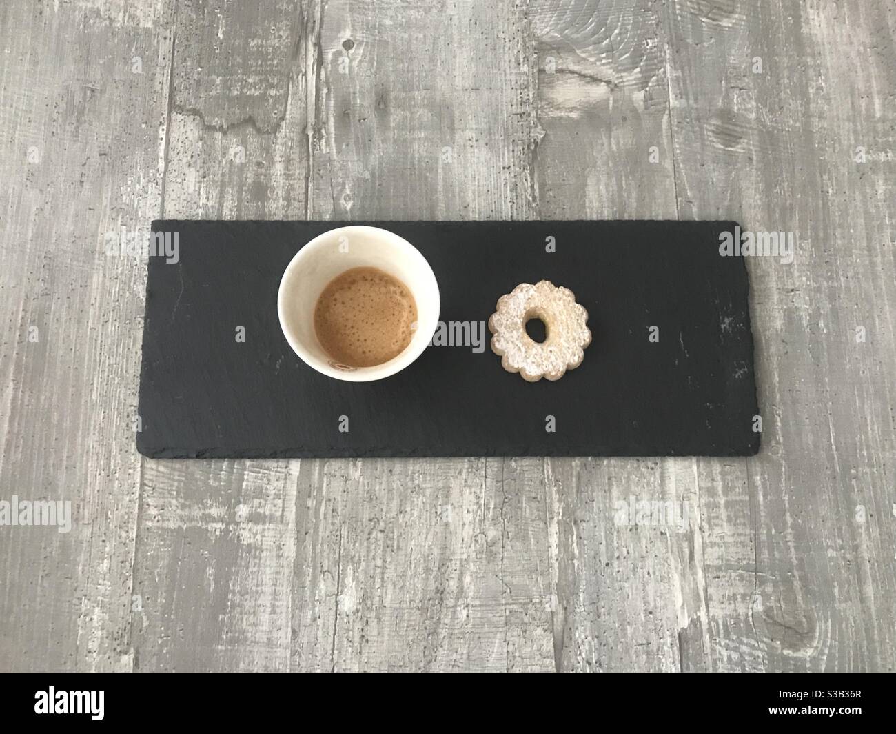 Espresso coffee and a biscuit served on a black slate against a wooden background - Smartphone Captured Stock Image