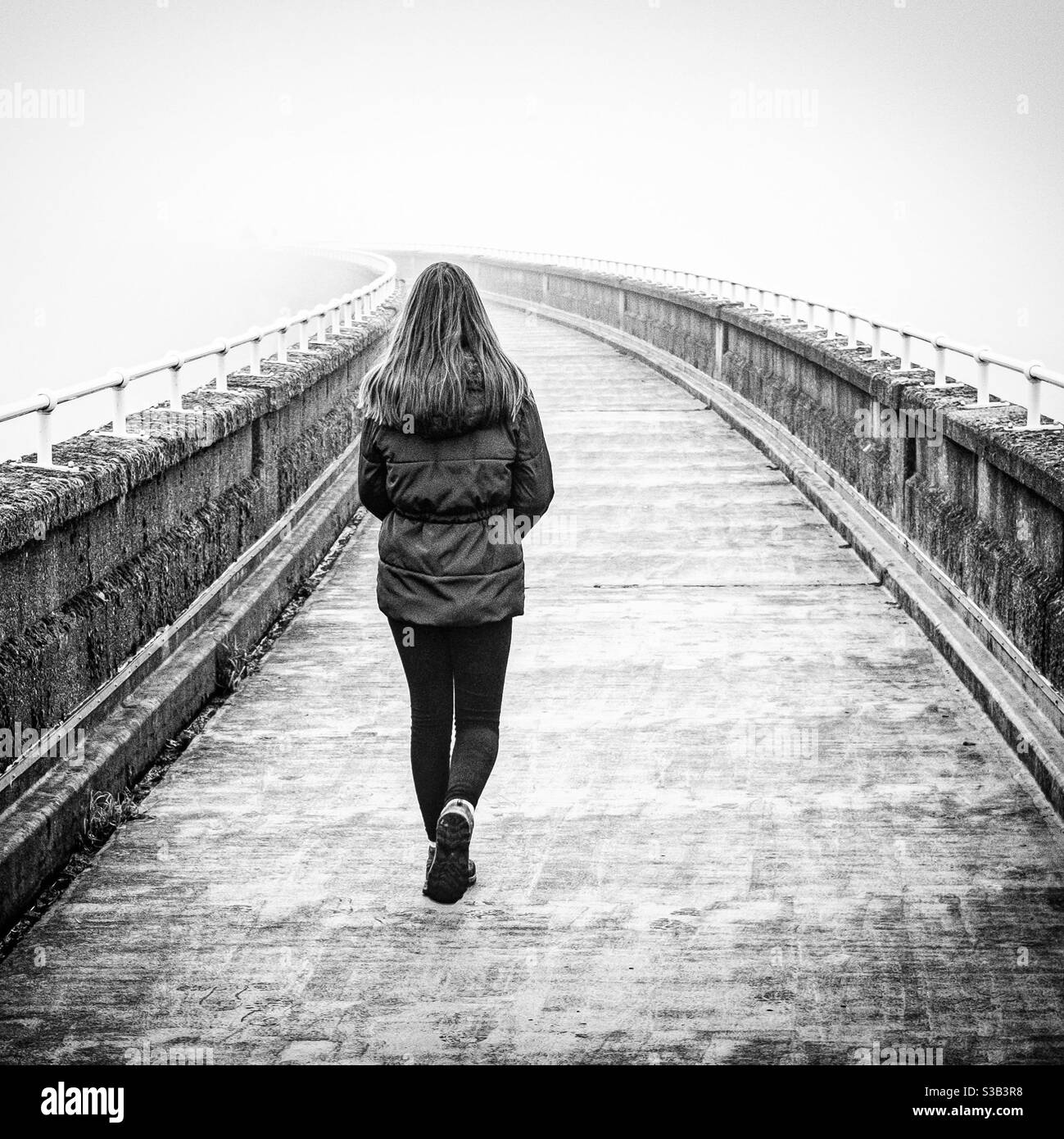 Girl walking across a dam in the fog. Stock Photo