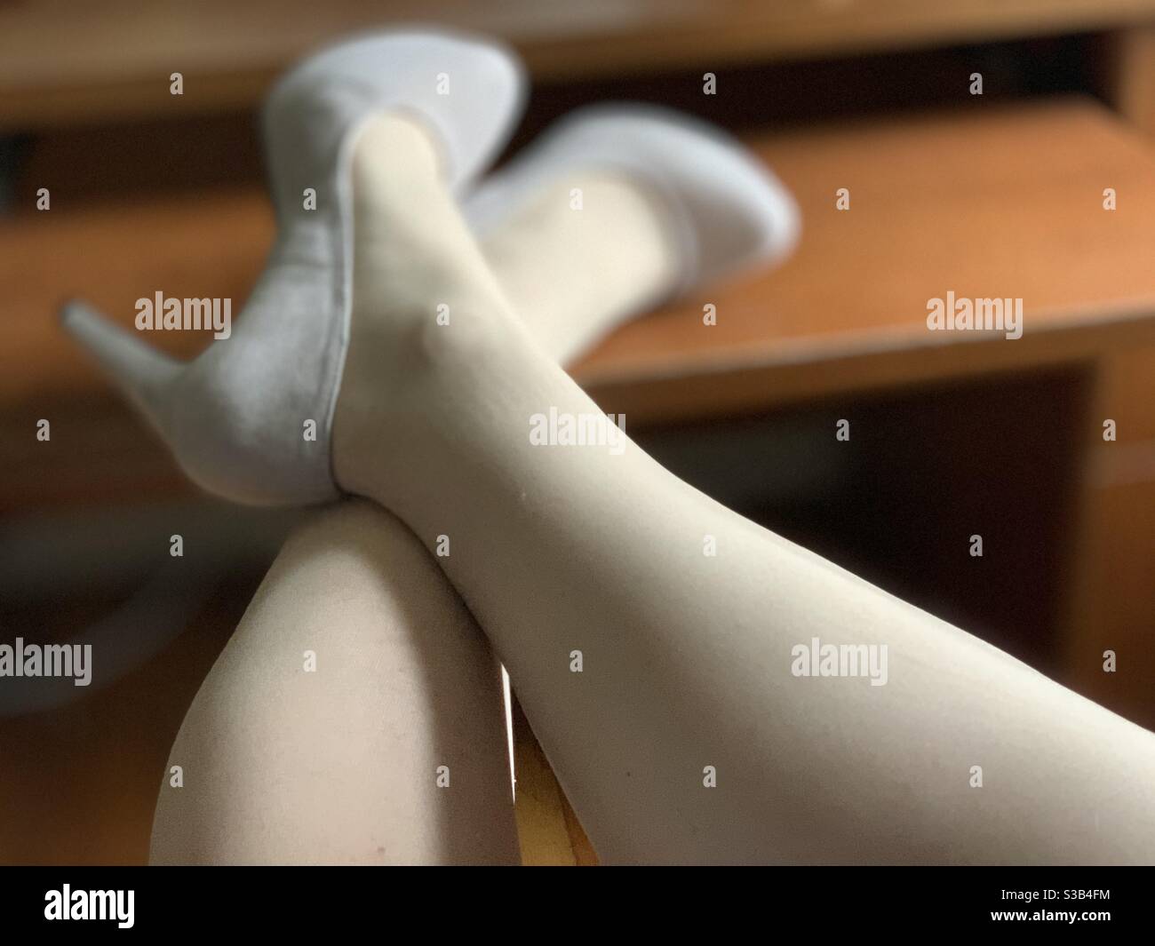 A woman’s crossed, stocking-clad legs and high heels on a desk - Smartphone Captured Stock Image