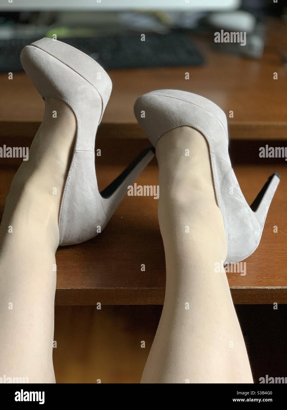 A woman’s stocking-clad legs and high heels on a desk - Smartphone Captured Stock Image