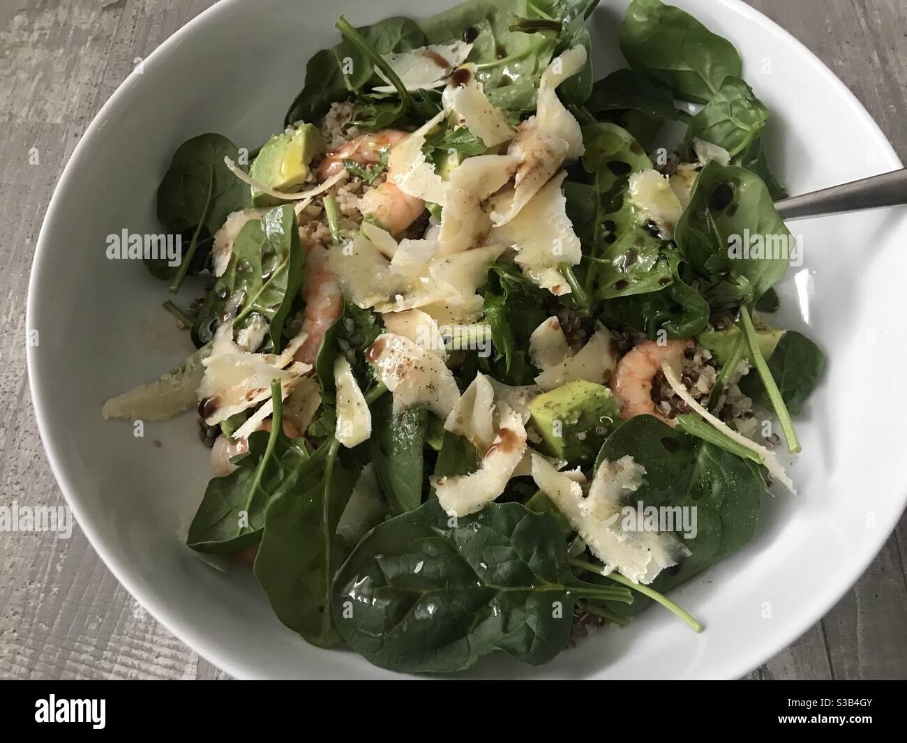 Quinoa, prawn, avocado and spinach salad topped with shavings of Parmesan cheese on a wooden background - Smartphone Captured Stock Image