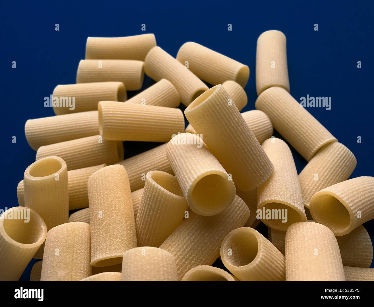 paccheri macaroni Italian dry raw pasta bronze drawn, pasta from Gragnano, Naples,Italy on blue background top view - Smartphone Captured Stock Image